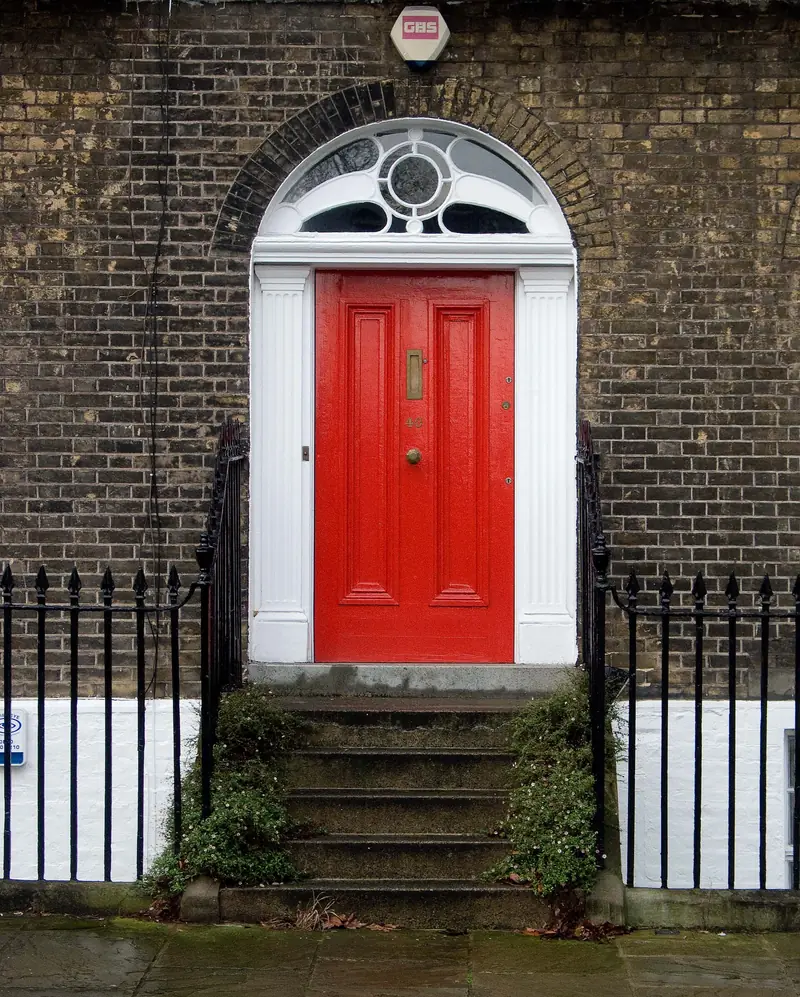 A red Georgian front door with a fanlight, black railings and stone steps on a London square